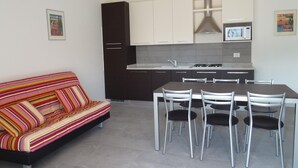 A modern kitchen with white cabinets, a dining table with chairs, and a colorful striped sofa. - Villa Faro Vecchio in Cavallino-treporti-formerly TUI Ferienhaus (Cavallino-Treporti)