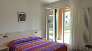 A hotel room with a bed, a small desk, a window with curtains, and a door leading to an outdoor area. - Villa Faro Vecchio in Cavallino-treporti-formerly TUI Ferienhaus (Cavallino-Treporti)