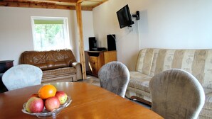 A dining area with a wooden table, a fruit bowl, a brown leather couch, and a patterned sofa. - Cottage in Szczecin by Puszcza Bukowa Park (Szczecin)