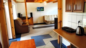 A cozy kitchen with a wooden ceiling, a television mounted on the wall, and a dining area with a table and chairs. - Cottage in Szczecin by Puszcza Bukowa Park (Szczecin)
