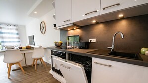 Una cocina moderna con armarios blancos, horno empotrado, lavavajillas y un lavamanos.
