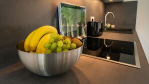 Una cocina moderna con un bol de acero inoxidable lleno de fruta en la encimera, una cafetera negra y un salpicadero de mármol.