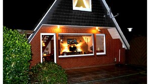 A house with a sloped roof, a chimney, and a window with curtains. - Ferienwohnung Tiefblick, Dornumersiel (Dornum)