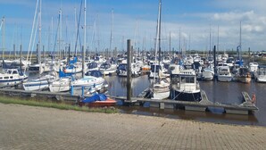A marina with numerous boats docked, wooden piers, and calm water. - Ferienwohnung Tiefblick, Dornumersiel (Dornum)