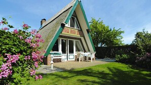 A thatched-roof house with a brick lower section, a green and white exterior, and a patio with white chairs. - Thatched Holiday Home in Freest With Terrace (Kröslin)