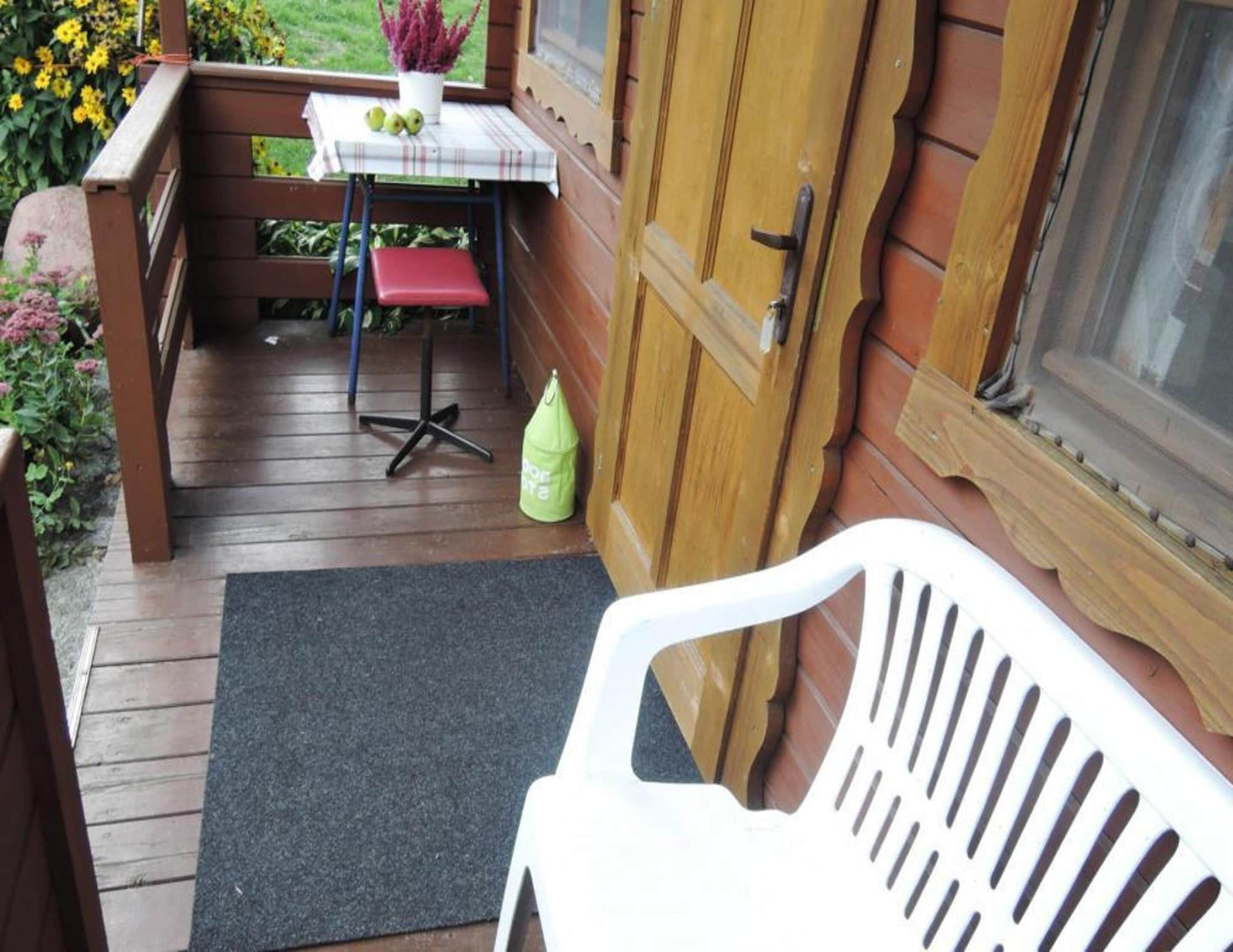 Une terrasse en bois avec une table et des chaises, un sac vert et une porte.