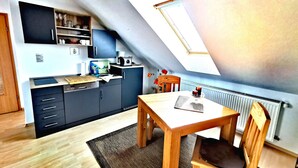 Cocina compacta con armarios oscuros, una mesa de madera y una silla. Un tragaluz ofrece luz natural.