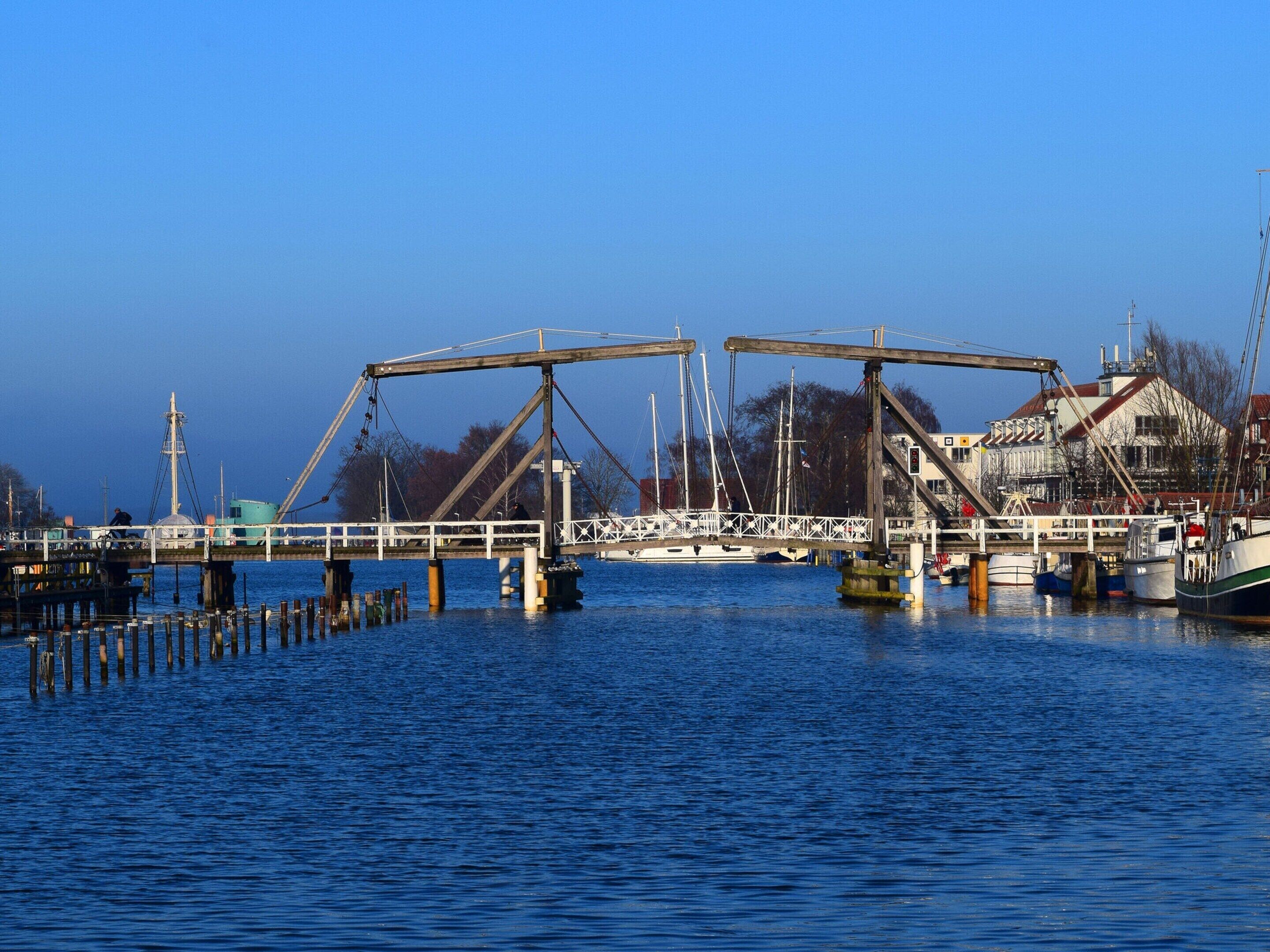 A pier with a crane and boats, a building with a red roof, and a clear blue sky.