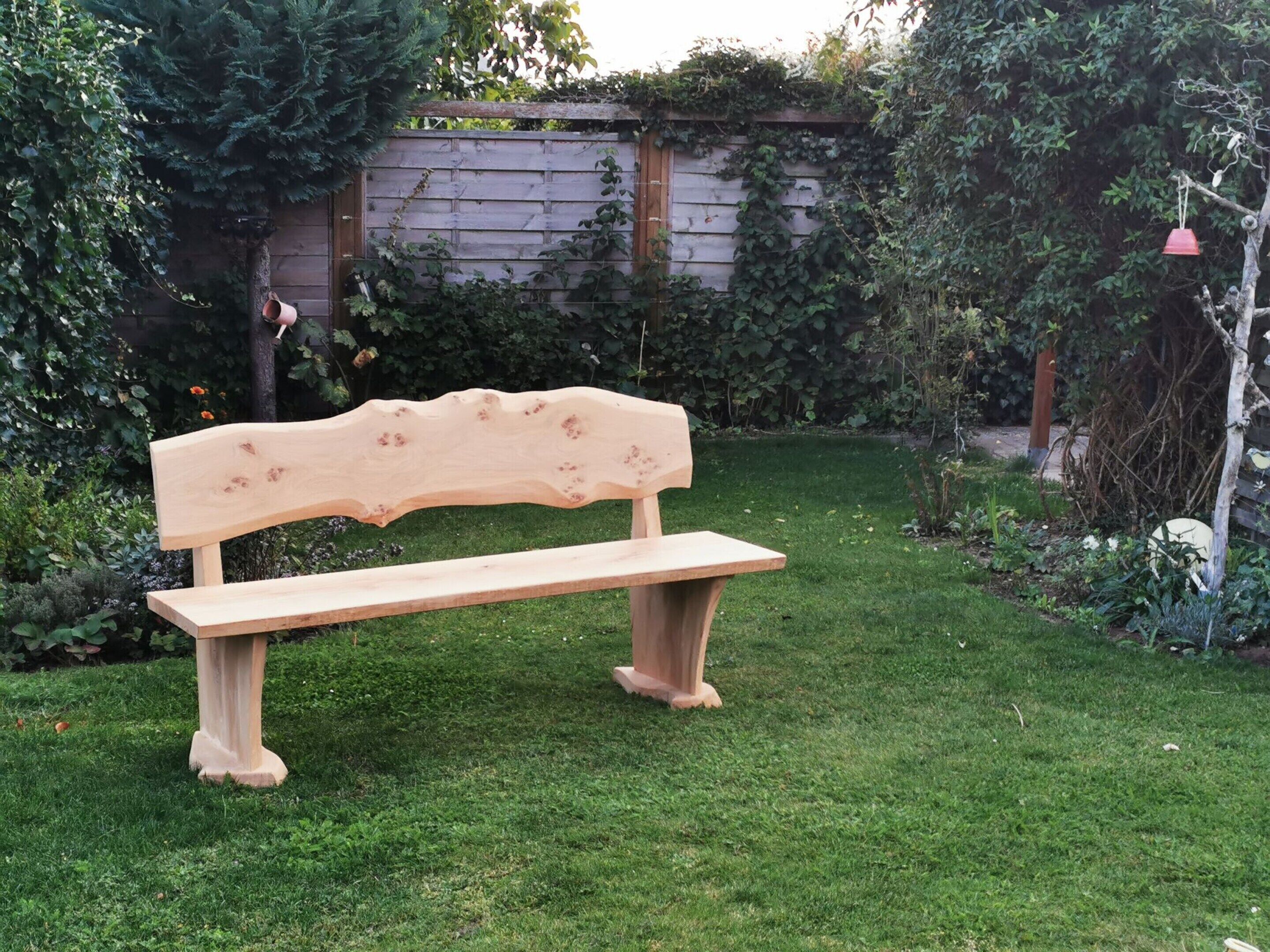 A wooden bench in a garden with a wooden fence and greenery in the background.