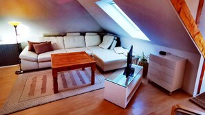 Una sala de estar estilo loft acogedora, con techo inclinado, un sofá blanco, una mesa de centro de madera y una mesita auxiliar con superficie de vidrio.