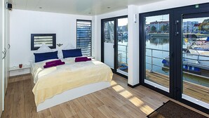 A modern bedroom with a large bed, a view of boats through the sliding glass door, and a wooden floor. - Haus in Ribnitz Damgarten for 3 Personen (Ribnitz-Damgarten)