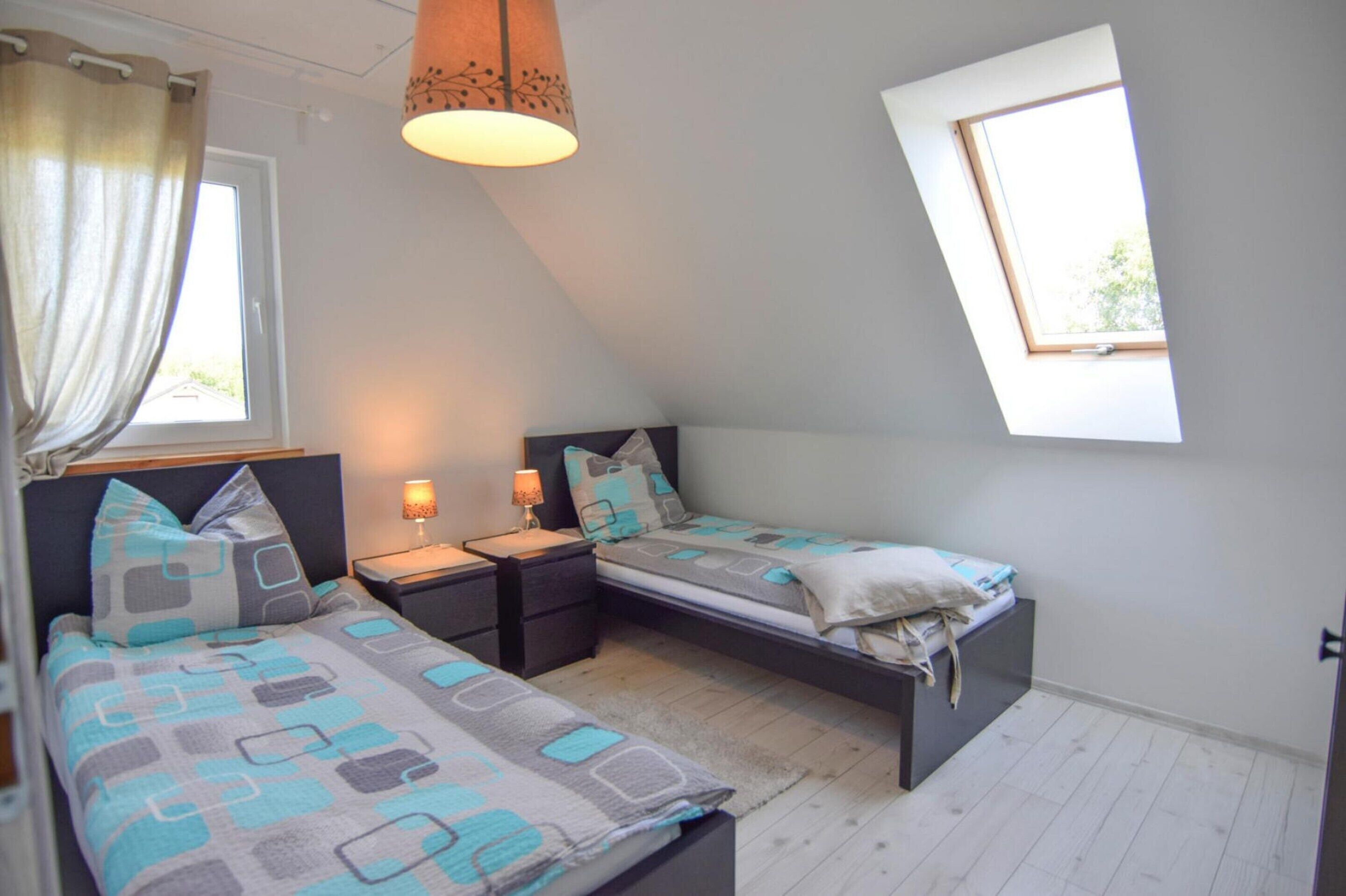 A small, well-lit room with two beds, a window, and a ceiling light.