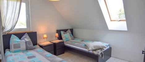 A small, well-lit room with two beds, a window, and a ceiling light.