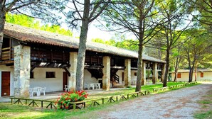 A rustic building with a tiled roof, wooden beams, and a covered porch with white plastic chairs. - Holiday Flat in the Belvedere Holiday Complex in Grado (Aquileia)