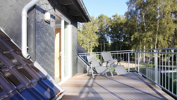 En balkong med ett trädäck, två vita loungestolar och ett metallräcke.
