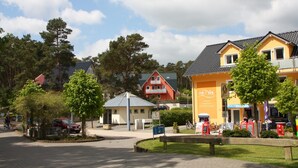 En gatubild med en gul byggnad, en röd byggnad och en liten lusthus. Det finns träd, en bänk och en cykel.