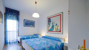 Ein Schlafzimmer mit zwei Betten, einem Fenster mit Vorhängen, einem Gemälde und einer Vase mit Blumen.