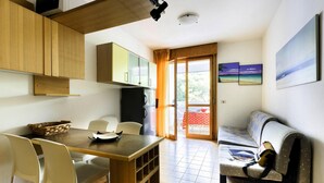 Eine kompakte Küche mit Holzausstattung, einem Esstisch mit Stühlen, einer Couch und einer Glastür zum Balkon.