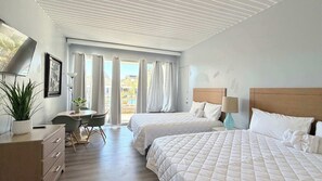 Habitación de hotel con dos camas, un escritorio, una silla, una planta en maceta y vistas al exterior.