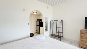 A bedroom with a bed, a wooden dresser, a TV, a wardrobe, and a kitchenette in the background. - SJ15 Cozy studio close to the beach (Myrtle Beach)