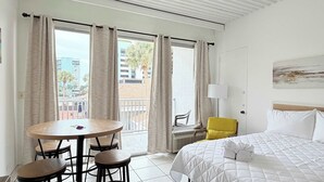 A hotel room with a bed, a round table with chairs, a yellow chair, and a balcony with curtains. - SJ15 Cozy studio close to the beach (Myrtle Beach)