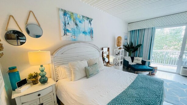 A bedroom with a bed, bedside tables, a nightstand, a mirror, a painting, a chair, and a view of the outdoors. - SJ20 Cozy studio close to the beach (Myrtle Beach)
