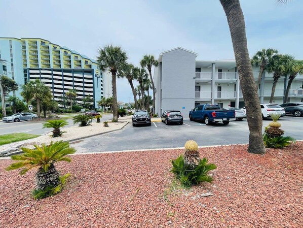 A parking lot with several cars, palm trees, and a building with multiple floors and balconies.