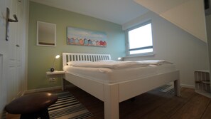 Ein Schlafzimmer mit Bett, Nachttischlampe, Fenster und einem Bild an der Wand.