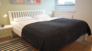 A bed with a white headboard, a black blanket, and a bedside table with a lamp. - Ferienwohnung in Wyk-boldixum auf Foehr (Wyk auf Foehr)