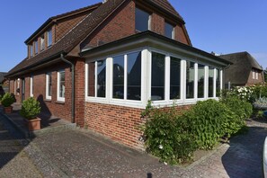 Een bakstenen huis met een groot erkerraam, bloempotten en een verharde oprit.