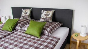 A bed with plaid bedding and decorative pillows, a bedside table with a lamp, and a small round table with a glass. - Ferienwohnung in der Nahe vom Hexentanzplatz (Thale)
