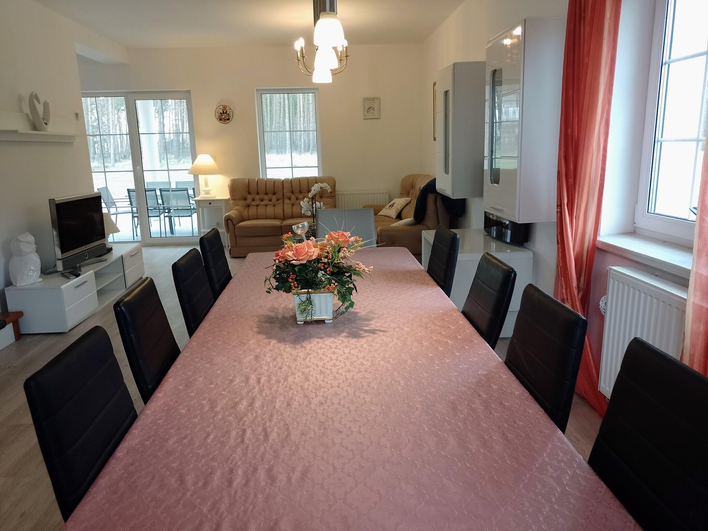 A spacious living room with a long dining table, a sofa, and a TV.