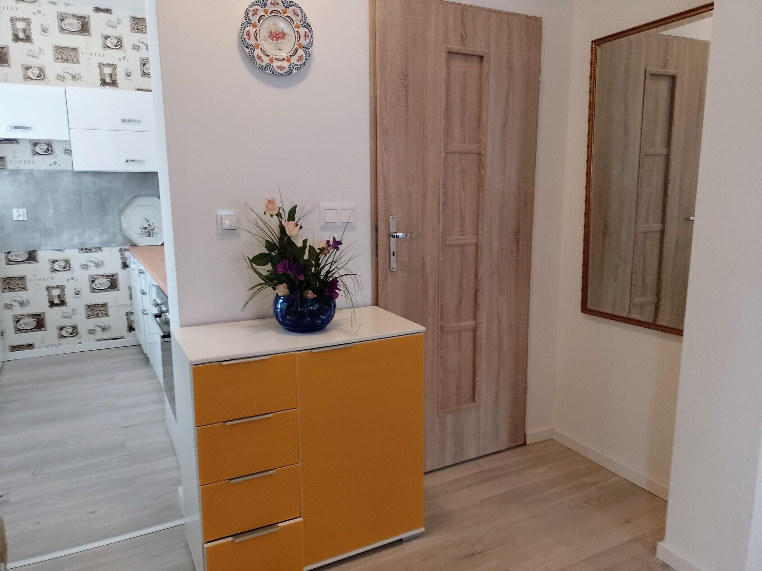 A room with a wooden wardrobe, a blue vase with flowers, and a door with a wooden frame.