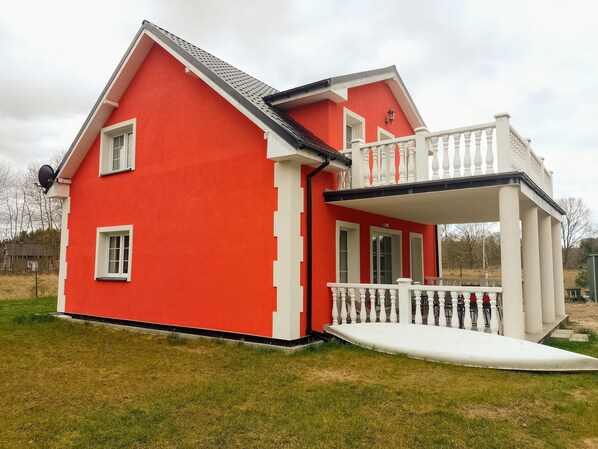 A red house with a white balcony and a small white porch. - Holiday Home in Nowe Warpno Near Harbor (Nowe Warpno)