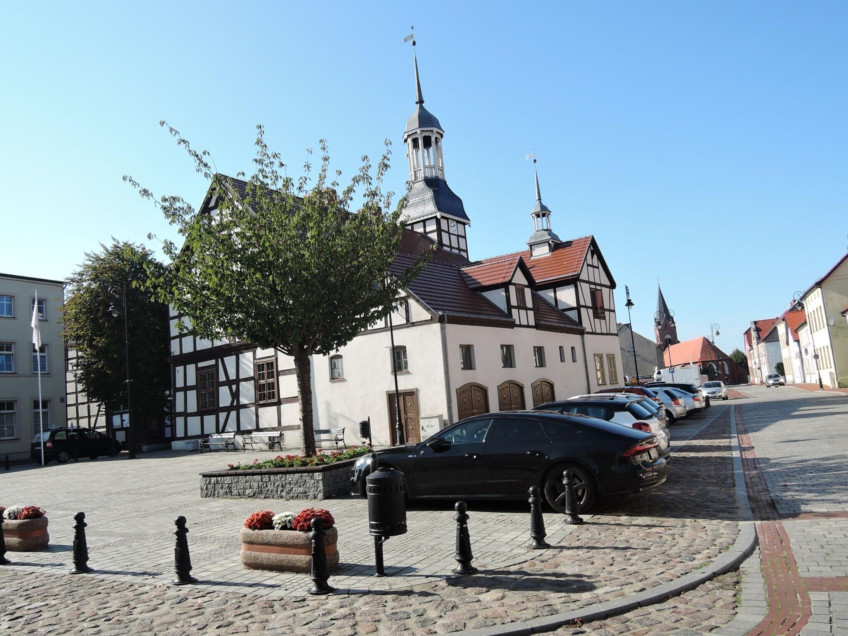 A cobblestone street with a historic building featuring a tower and a church in the background.