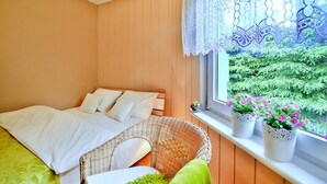 Ein Schlafzimmer mit einem Bett, einem Korbstuhl und einem Fenster mit Pflanzen.