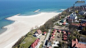 An aerial view of a coastal area with a sandy beach, residential buildings, and a pier extending into the sea. - Comfortable Ground Floor Apartment, Summer Pool (Postomino)