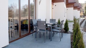 A modern outdoor patio with a glass door leading to a seating area, a table with chairs, and a small garden. - Comfortable Ground Floor Apartment, Summer Pool (Postomino)