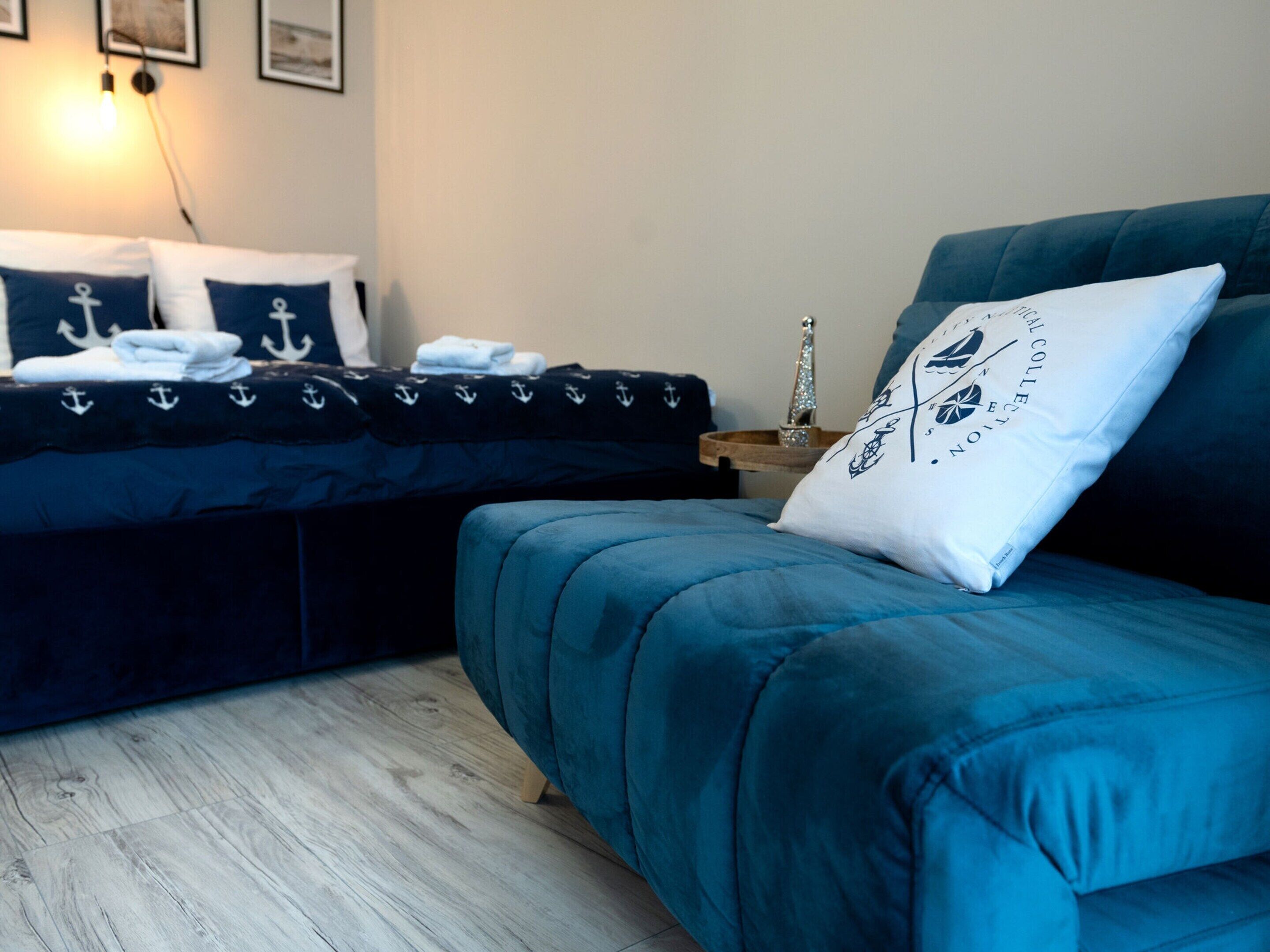 A room with a bed featuring navy blue bedding with anchor designs, a matching navy blue sofa, and a small bedside table with a decorative item.