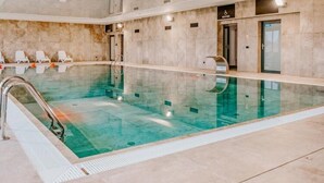 A large indoor swimming pool with clear water, a metal pool ladder, and lounge chairs along the side. - Air-conditioned Apartment, Indoor Pool, Sauna (Dziwnów)