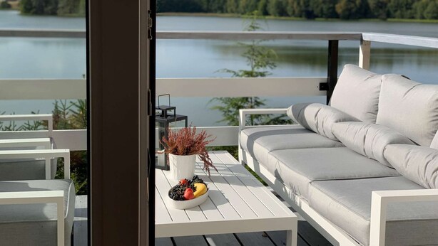 Un balcon avec un canapé blanc, une petite table sur laquelle se trouve un panier de fruits et une plante en pot.