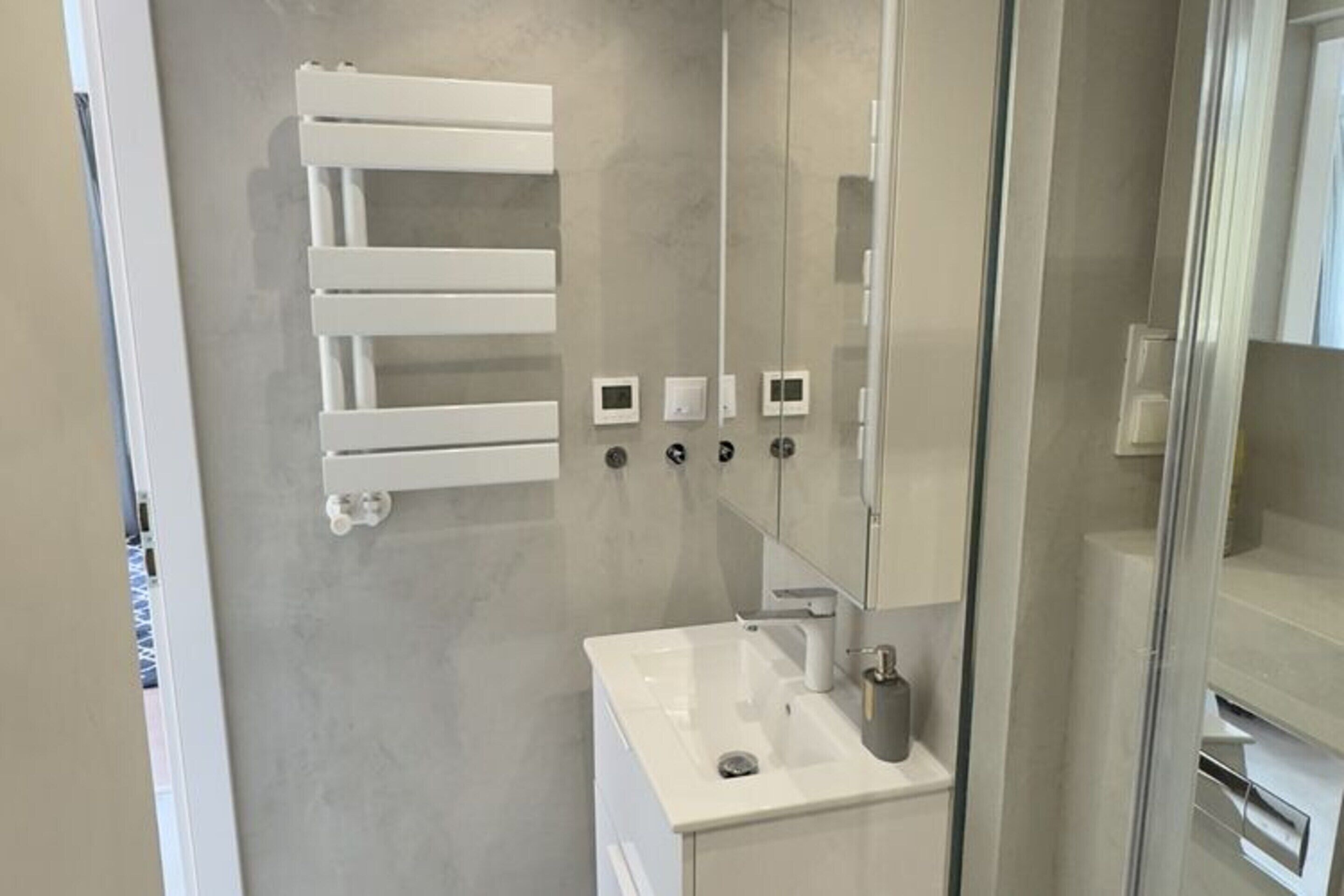 A modern bathroom with a glass shower enclosure, a white sink, and a towel rack.