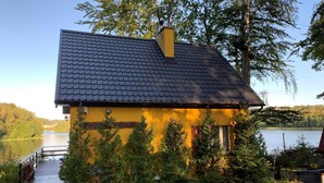 Un bâtiment jaune, surmonté d’un toit en tuiles sombres, entouré de verdure et bordé d’un lac.