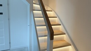 Un escalier avec des marches en bois et une rampe blanche, menant à une porte sur laquelle est accrochée une petite image.