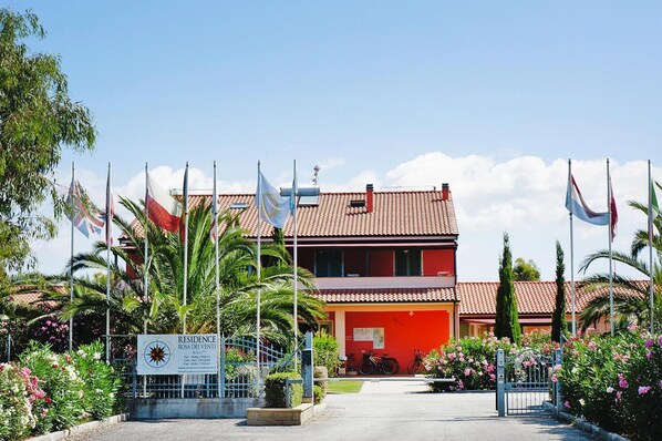 A building with a red facade, multiple flags, and a sign indicating 'Residence Rosa dei Venti'.