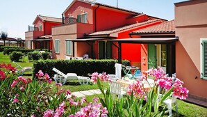 A two-story house with a red facade, a balcony, and a garden with pink flowers. - Apartment in Tuscany Near Sandy Beaches (Rosignano Marittimo)