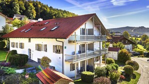 Una casa a due piani con un tetto in tegole rosse, un balcone e un giardino curato.