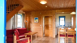 A wooden interior with a sofa, table, chairs, a staircase, and a kitchen area. - Ferienpark Harz in Hasselfelde (Oberharz am Brocken)
