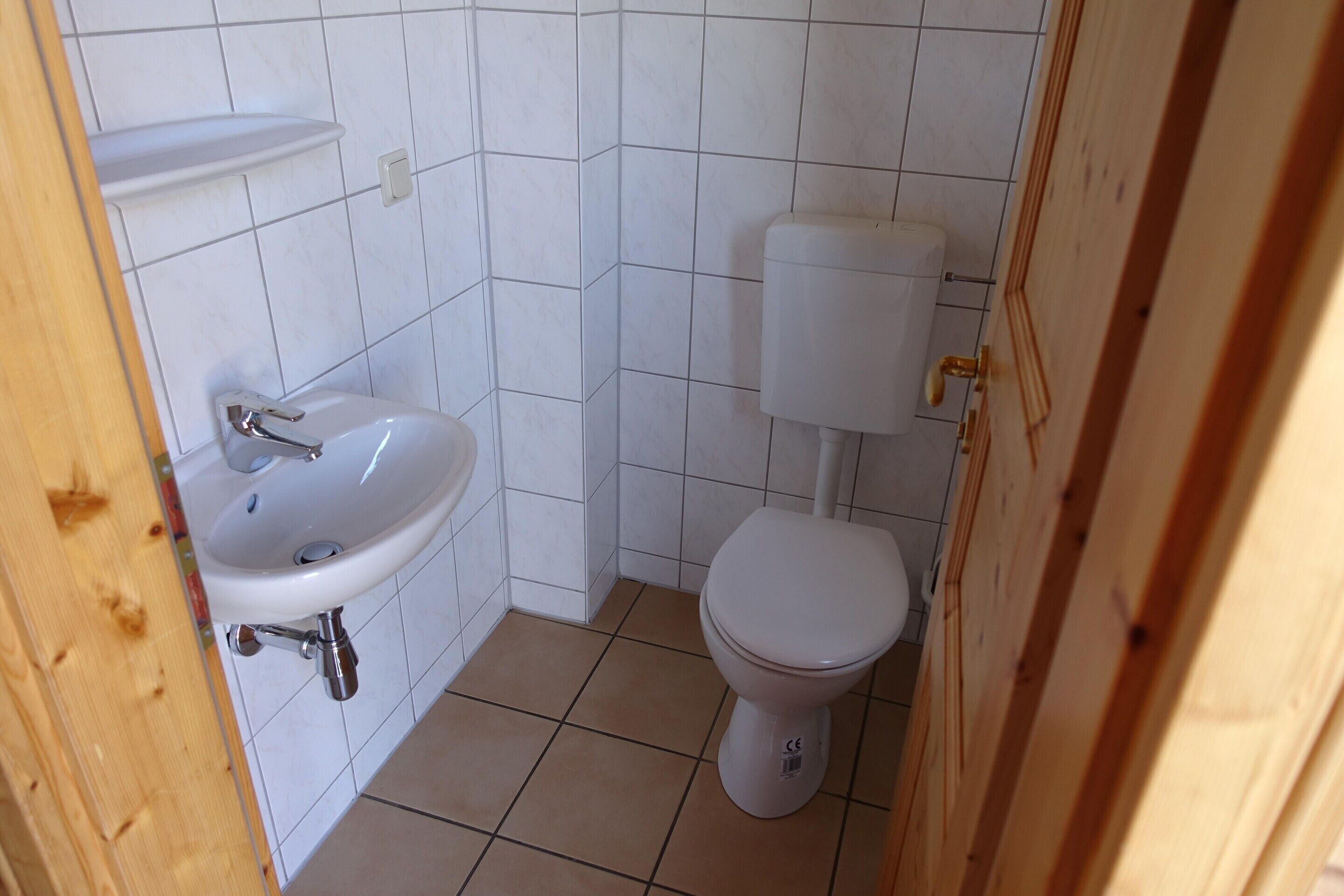 A small bathroom with a white sink, toilet, and tiled walls.