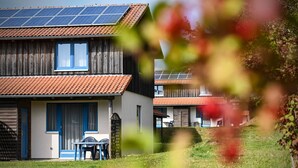 A two-story house with solar panels, a wooden exterior, and a small patio with a table and chairs. - Ferienpark Harz in Hasselfelde (Oberharz am Brocken)